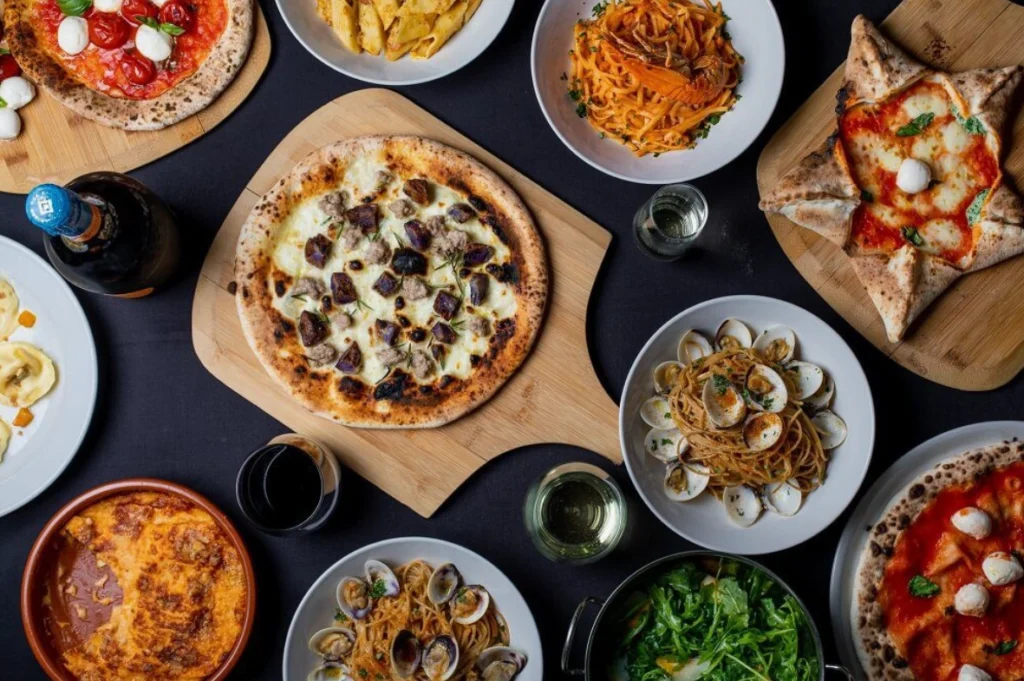 Traditional Pisa dishes including pizza, seafood pasta, and lasagna on a rustic black table